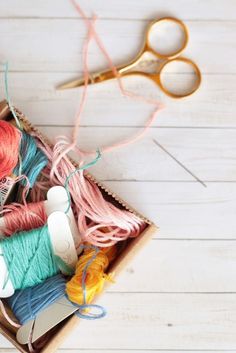 an open box with yarn, scissors and thread in it on a white wooden surface