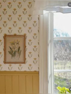 a painting hangs on the wall next to a window in a room with floral wallpaper