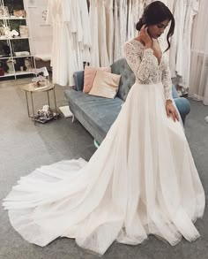 a woman standing in front of a couch wearing a white wedding dress with long sleeves