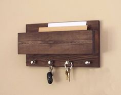 a wooden key holder with two keys hanging from it's sides and a note pad on the other side