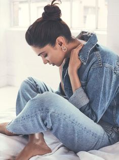 a woman sitting on top of a bed wearing jeans