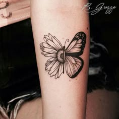 a black and white butterfly tattoo on the right arm, with a daisy in it's center