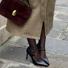 a woman in high heels is holding a burgundy purse and black tights with her legs crossed