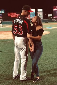 a man and woman standing next to each other on top of a baseball field at night