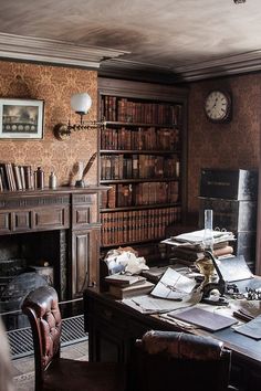 an old fashioned desk with lots of books on it and a fireplace in the corner