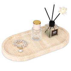 a white tray with two candles and a necklace on it next to a bottle of perfume