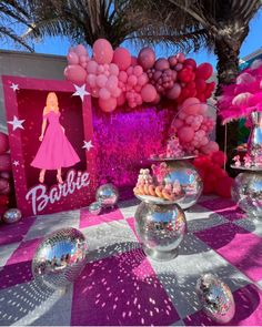 a table topped with lots of pink and silver balloons covered in confetti next to a barbie sign