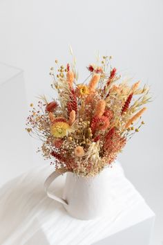 an arrangement of dried flowers in a white vase