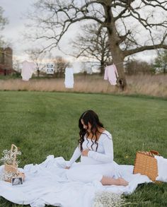 a woman sitting on top of a white blanket in the grass next to a tree