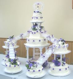 three tiered wedding cake with purple and white flowers on it sitting on top of a table