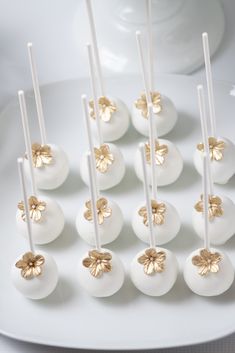 white cake pops with gold flowers on them sitting on a plate next to a cup and saucer