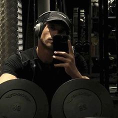 a man wearing headphones and holding a cell phone in front of some dumbbells