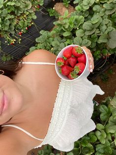 a woman holding a bowl of strawberries in front of her face while laying on the ground