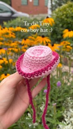 a hand holding a pink crocheted hat in front of yellow flowers with the words taradal tiny cowboy hat?