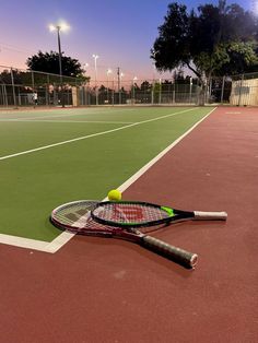 a tennis racket and ball are on the court at night with lights in the background