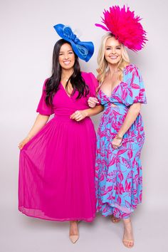 two women standing next to each other in dresses and hats