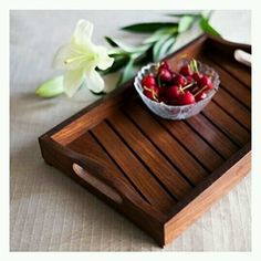 a bowl of cherries on a wooden tray next to white flowers and green leaves