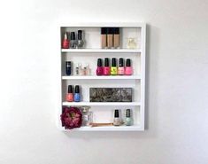 a white shelf filled with nail polish bottles and cosmetics on it's sides next to a toilet