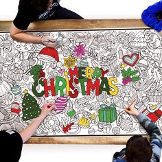 three people drawing on a large christmas poster