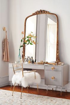 a dressing table with a mirror, stool and vase on it in a white room