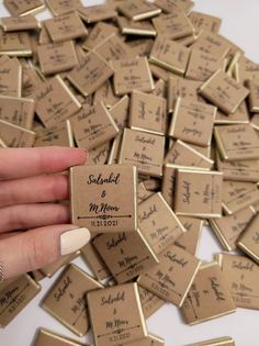 a person is holding up some small tags with names on them, and there are many smaller ones in the background