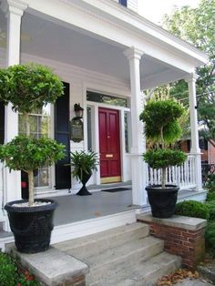 two potted plants sit on the front steps of a white house with red door