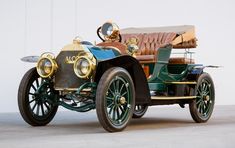 an old fashioned car is parked in front of a white wall