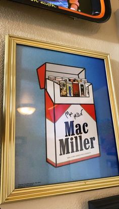 an advertisement for mac miller is hanging on the wall next to a framed poster with images of people in a carton