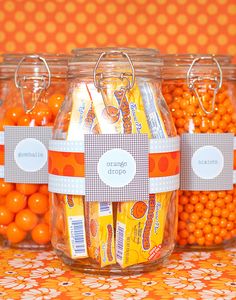 three jars filled with candy sitting on top of a table next to orange candies