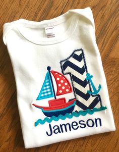 Boys Sailboat Birthday shirt! Sailboat in red, teal blue and navy with age appliqued in navy chevron. Teal blue Ric rac finishes off the design with name embroidered below in navy thread. Prefer another color combination...just message me with your requests! Onesie Sizes 6-12mo 17-24lbs 12-18mo 25-29lbs Boys Tee Sizes (100% Cotton) 12mo 11W x 13L 18mo, 11.5L x 14.5L 2T, 12W x 15.5 3T 12.5 W X 16.5L 4T 13w x 17L 6T 13.5W x 19.5L YSM (6-8) YMED 10-12 | Sailboat Birthday Shirt, 1St Birthday Ideas, Sailboat Birthday, 1st Birthday Ideas, Sailing Party, Kids Boat, Nautical Birthday, Boys Tops, Baby Cakes, Ric Rac, Kids Clothes Boys