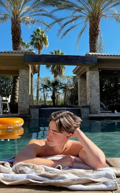 a man laying on top of a towel next to a swimming pool with palm trees