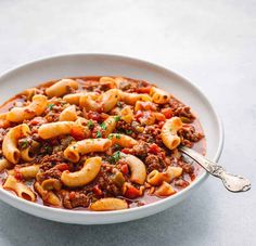 a white bowl filled with pasta and meat sauce on top of a gray countertop