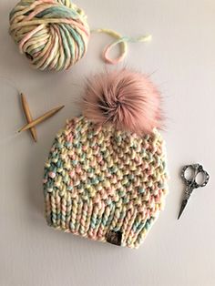 a knitted hat with two balls of yarn next to it and scissors on the table