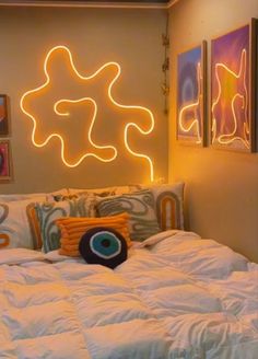 a bed with white comforter and pillows in front of a neon sign on the wall