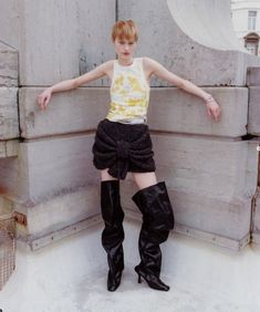 a young woman in black boots standing next to a wall