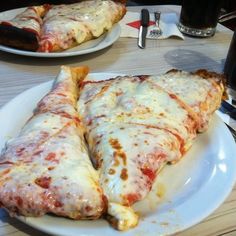 two slices of pizza on a white plate next to a glass of soda and fork