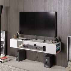 a flat screen tv sitting on top of a white shelf next to speakers and books