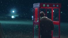 a man standing in front of a red phone booth on a snowy day at night