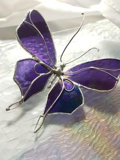 a purple glass butterfly sitting on top of a white table cloth with an intricate design