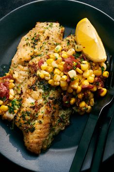 a black plate topped with chicken and corn next to a lemon wedge on top of a fork