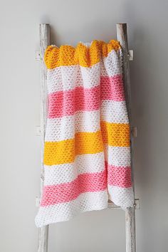 a crocheted blanket sitting on top of a wooden chair next to a white wall