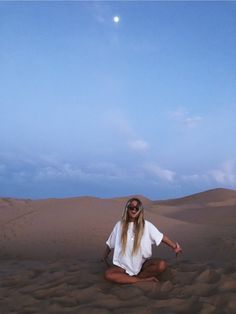 a woman sitting in the middle of a desert with her eyes closed and hands out