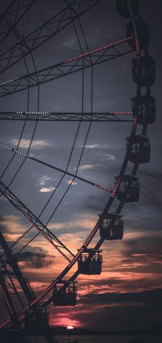 a ferris wheel with the sun setting in the background and some lights on it's sides