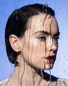 a woman standing in front of a window with rain drops on her face and hair