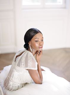 a woman sitting on top of a bed wearing a white dress and holding her hand under her chin