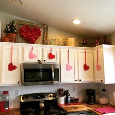 a kitchen with white cabinets and red hearts hanging from the wall above the stove top