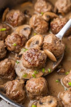 a ladle full of meatballs and mushrooms with green onions in a broth