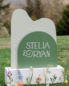 a sign that says stella and ryan on it in the middle of some grass with flowers around it