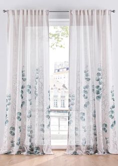 an open window with white curtains and blue flowers on it, in front of a wooden floor