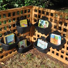 several books are placed in black baskets on the side of a wooden fence with trees behind them